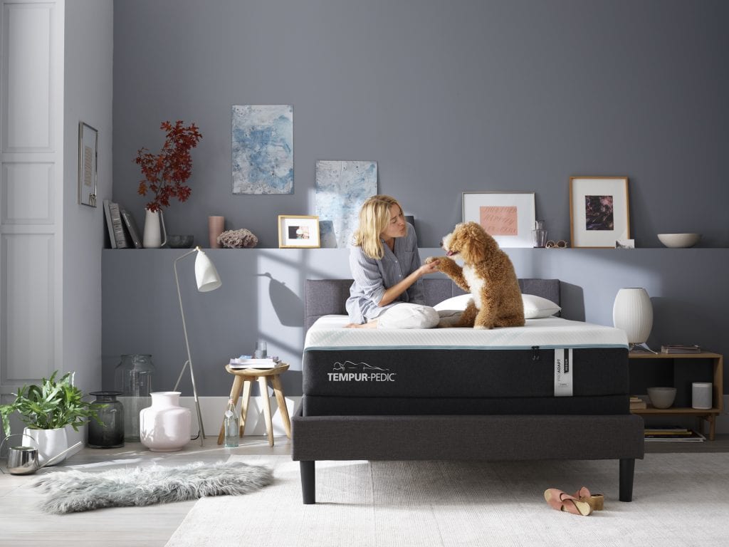 Woman sitting on a Tempur-Pedic mattress with her dog.