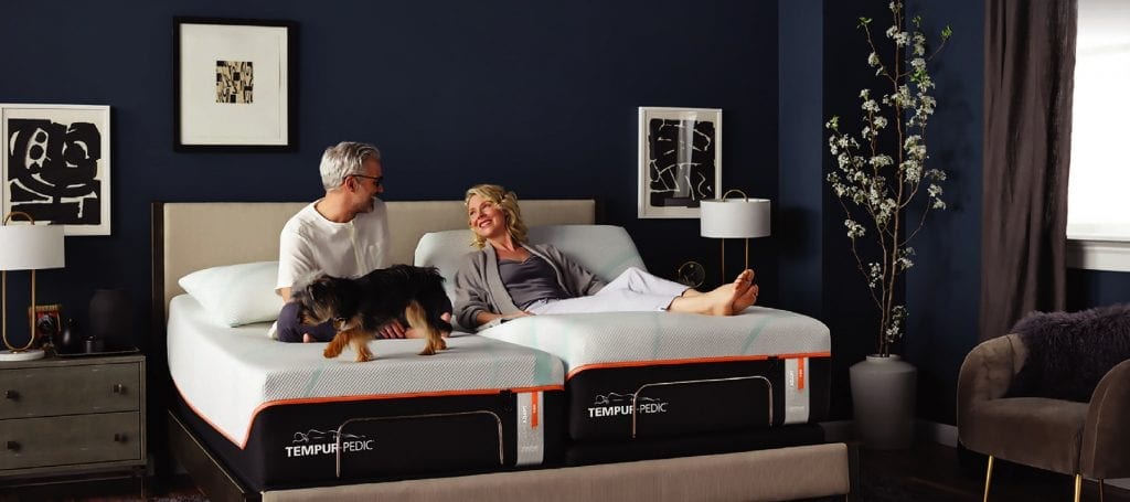 an older couple sitting on a Tempurpedic mattress with their puppy