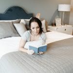 Woman lays atop a bed reading a book. She purchased the best mattress online.