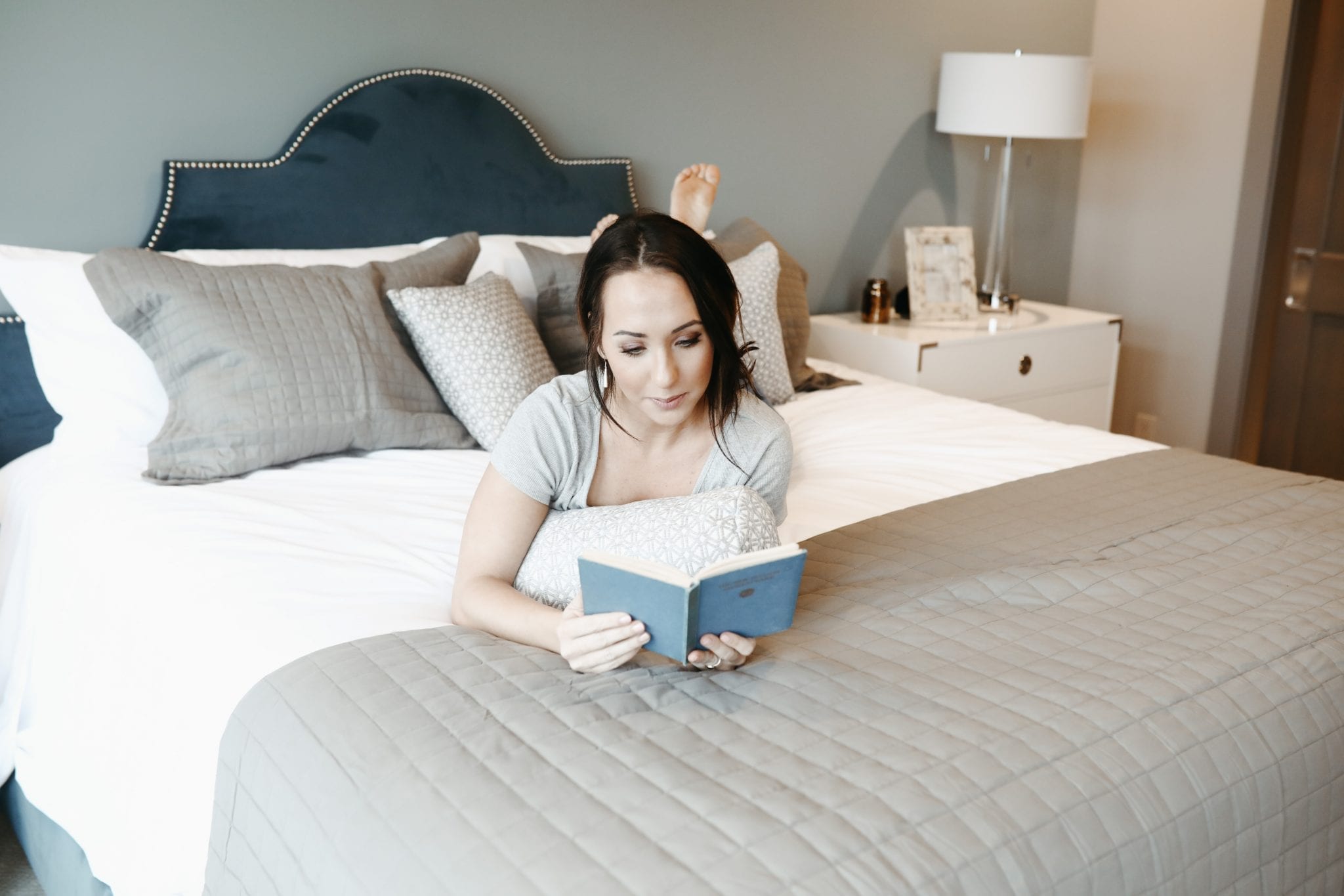 Woman lays atop a bed reading a book. She purchased the best mattress online.