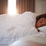 Woman asleep on twin bed as moring light breaks through curtains