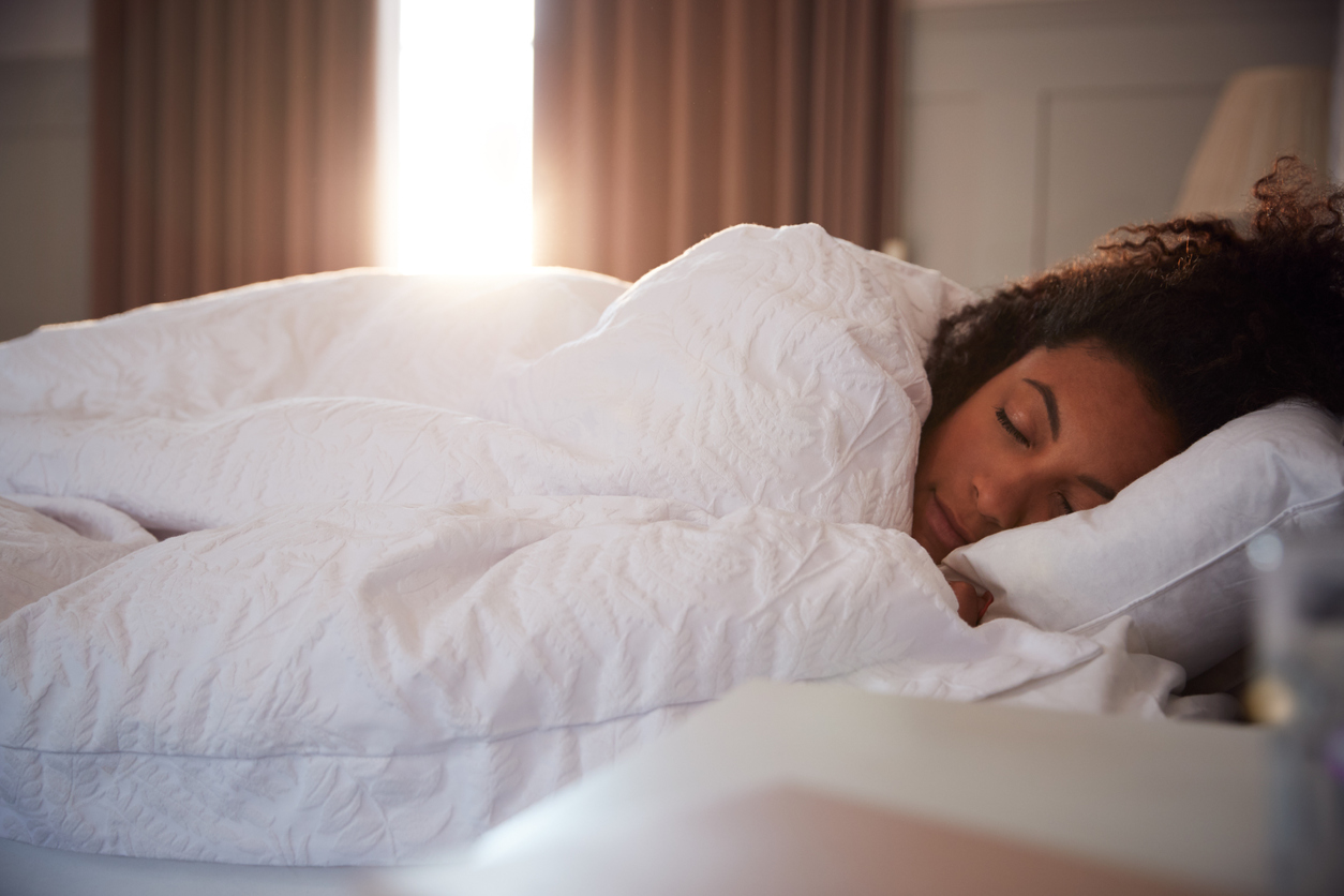 Woman asleep on twin bed as moring light breaks through curtains