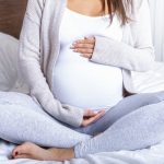 Pregnant woman sitting on a bed holding her belly