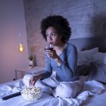 Woman eating popcorn, drinking wine, watching TV before bed
