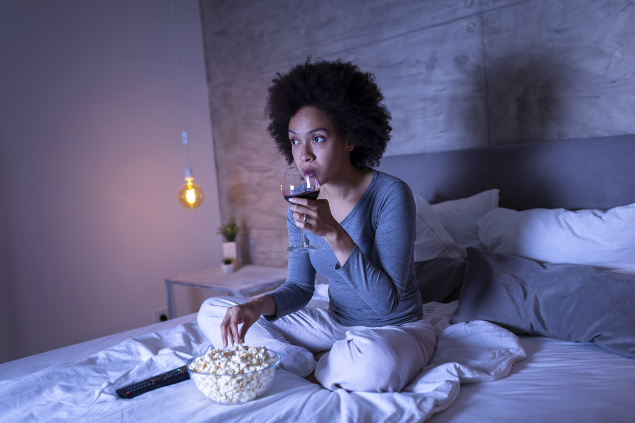 Woman eating popcorn, drinking wine, watching TV before bed